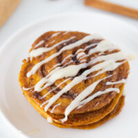 pumpkin cinnamon roll pancakes on plate with cream cheese glaze on top