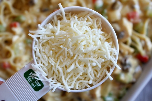 cup of shredded cheese in a white measuring cup above a casserole