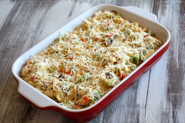 chicken spaghetti casserole in a red and white casserole dish ready for the oven