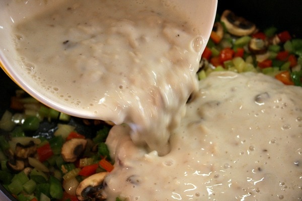 Chicken Spaghetti Casserole recipe from RecipeGirl.com #chicken #spaghetti #casserole #recipe #RecipeGirl pouring sauce into vegetables in a skillet to make the sauce for chicken spaghetti casserole