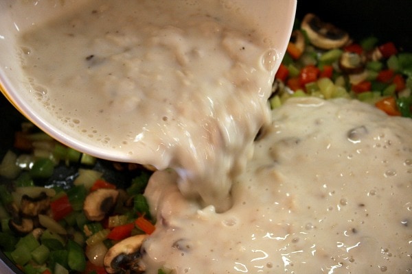 pouring sauce into vegetables in a skillet to make the sauce for chicken spaghetti casserole