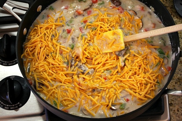 Chicken Spaghetti Casserole recipe from RecipeGirl.com #chicken #spaghetti #casserole #recipe #RecipeGirl adding cheese to the sauce for chicken spaghetti casserole in a skillet