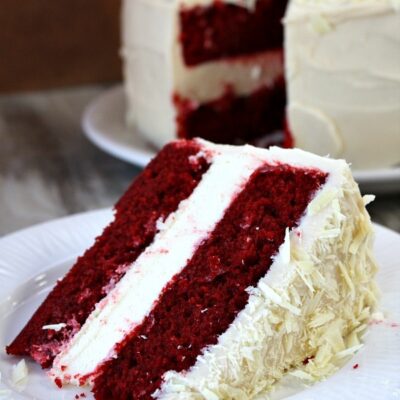 slice of red velvet cheesecake cake on a white plate with the cake in the background