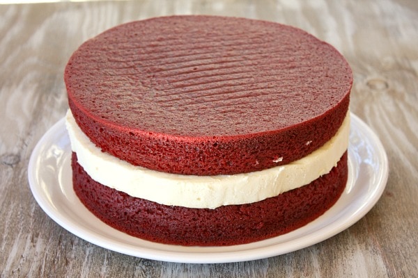 two layers of red velvet cake with a layer of cheesecake in the middle on a white plate