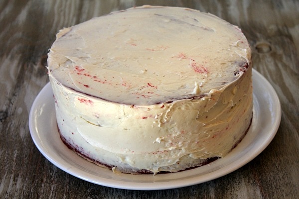adding first layer of frosting to a red velvet cake on a white plate
