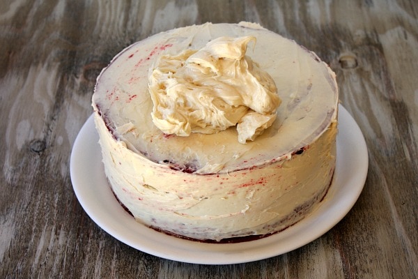 adding frosting to a red velvet cake