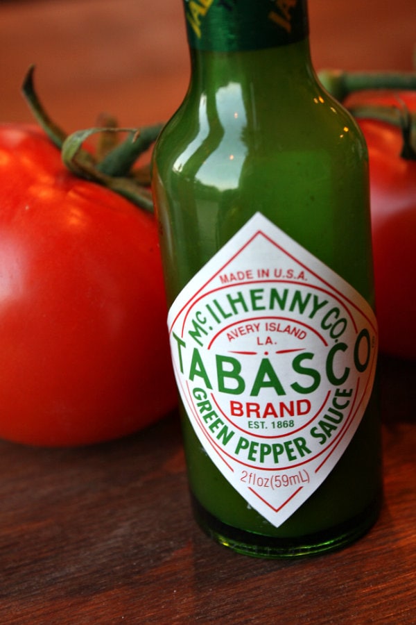 a bottle of green tabasco sauce with a tomato behind it