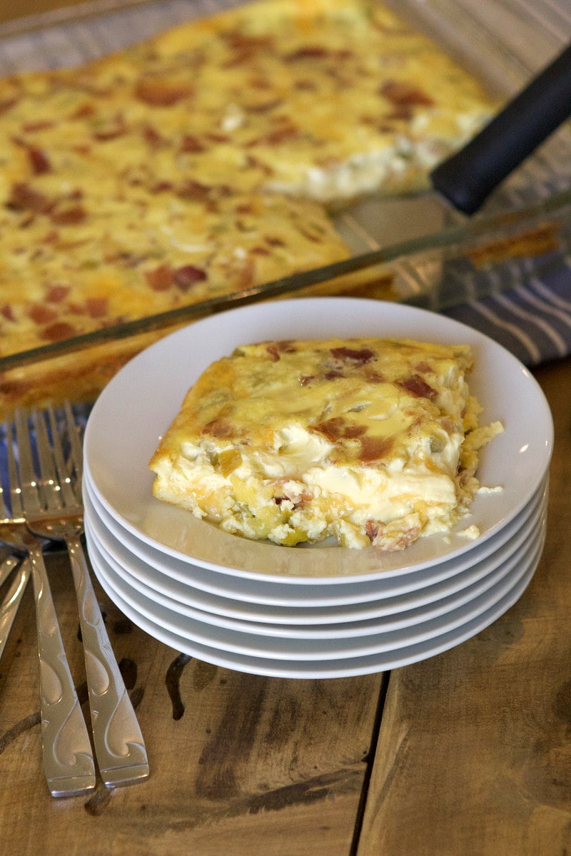 single serving of egg casserole sitting on the top plate of a stack of white plates. Forks on the side. Casserole in the background