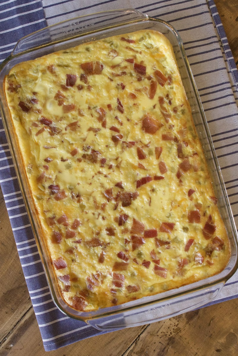 green chile bacon and cheese egg bake in a casserole dish sitting on a blue and white striped napkin