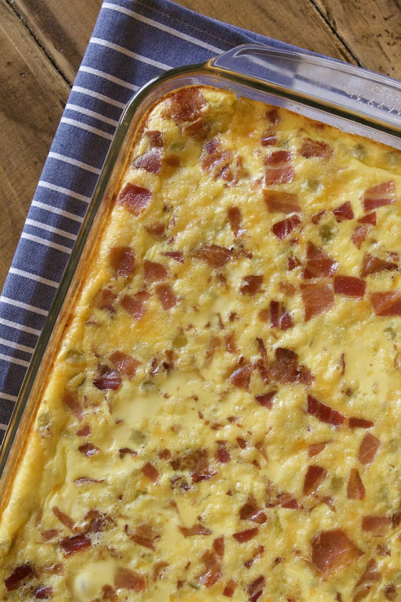 Green chile bacon and cheese egg bake in a pyrex casserole dish on a blue and white striped cloth napkin