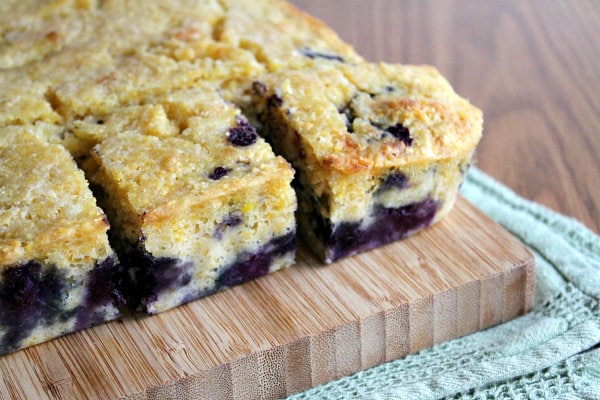 blueberry cornbread cut into pieces on a cutting board set on a green cloth napkin