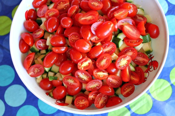 tomato added to a bowl of zucchini and corn set on a blue and green polka dot tablecloth