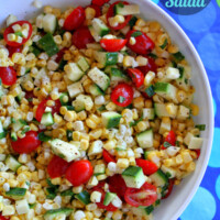 overhead shot of fresh corn, tomato and zucchini salad in a white bowl, set on a blue and green striped tablecloth