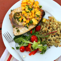 grilled swordfish with pineapple peach salsa and salad and rice on a plate