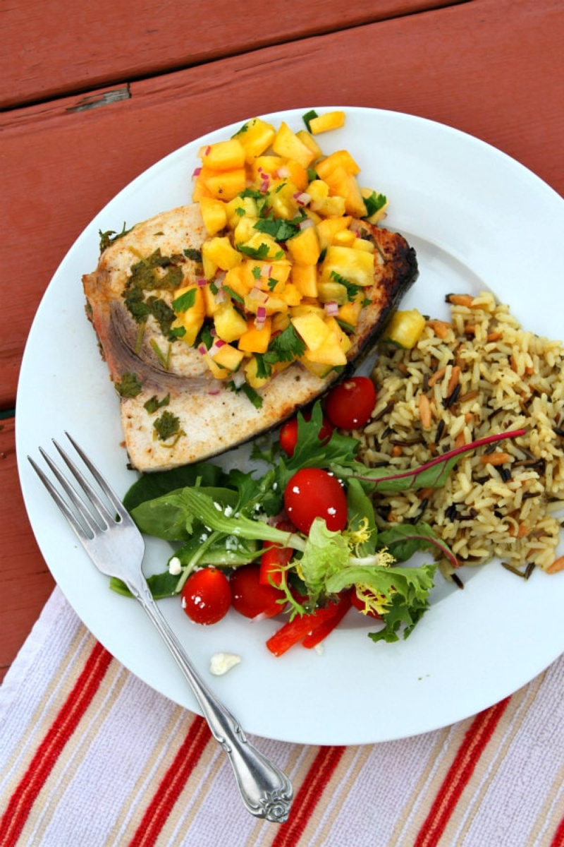 grilled swordfish with pineapple peach salsa and salad and rice on a plate