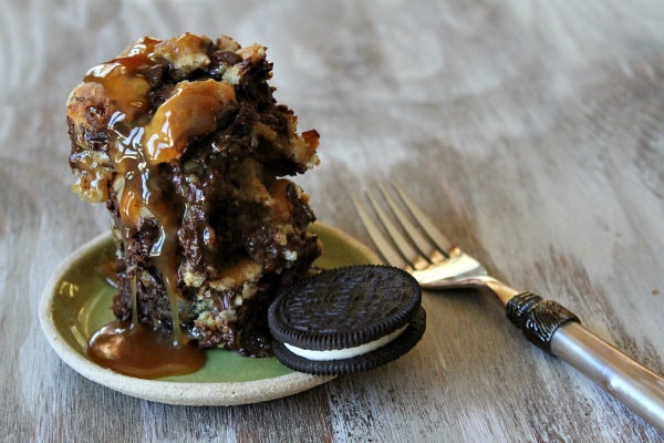 Oreo and Caramel Stuffed Chocolate Chip Cookie Bar hot out of the oven on a green plate covered with caramel and served with an oreo with a fork on the side