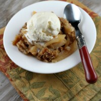 apple crisp topped with ice cream in a white bowl