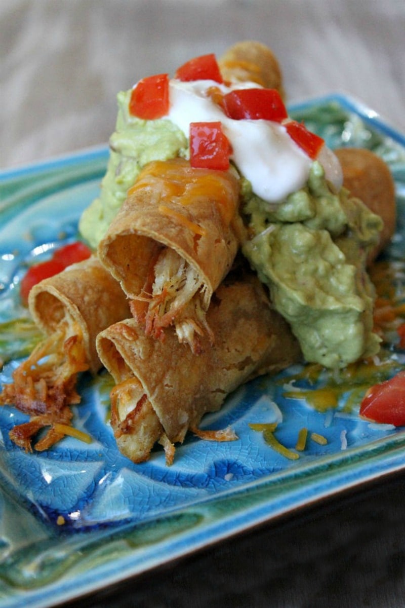 Easy Baked Chicken Taquitos garnished with sour cream and guacamole on a blue and green decorative plate