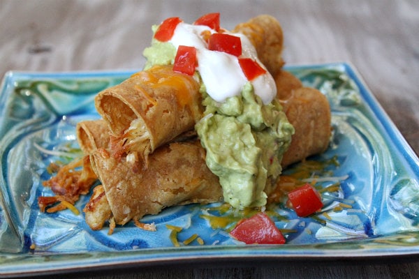 Easy Baked Chicken Taquitos garnished with sour cream and guacamole on a blue and green decorative plate