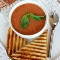 bowl of tomato soup with fresh basil and grilled sandwich on side