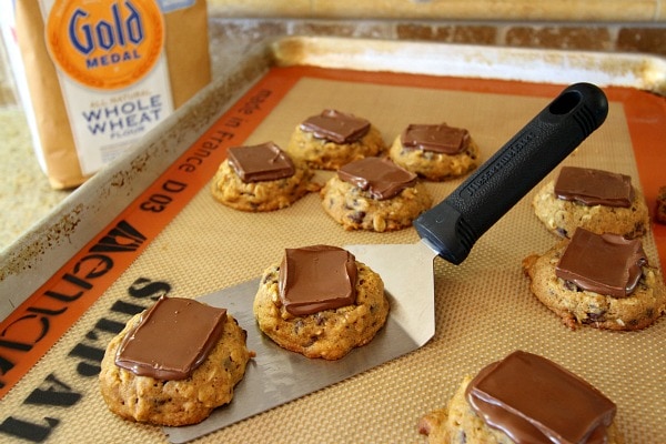 Pumpkin Oatmeal Candy Bar Cookies recipe from RecipeGirl.com #pumpkin #oatmeal #candy #candybar #chocolate #cookies #recipe #RecipeGirl Pumpkin oatmeal candy bar cookies on a baking sheet with a spatula