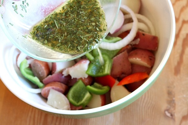 Pouring herb mixture onto sausage peppers and potatoes