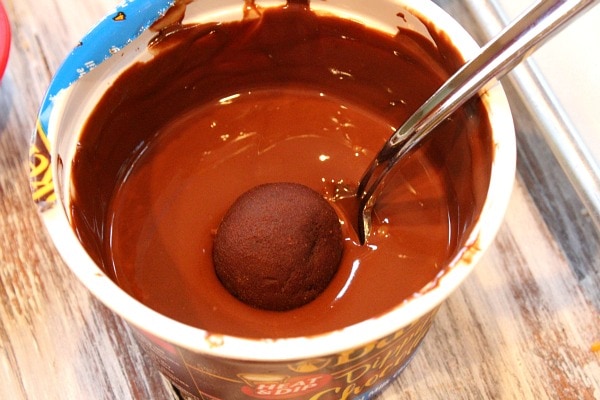 chocolate chocolate chip cookie dough dipped in a tub of melted chocolate with a spoon