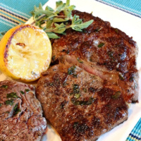 pan fried lemon-garlic rib-eye steaks on a white plate