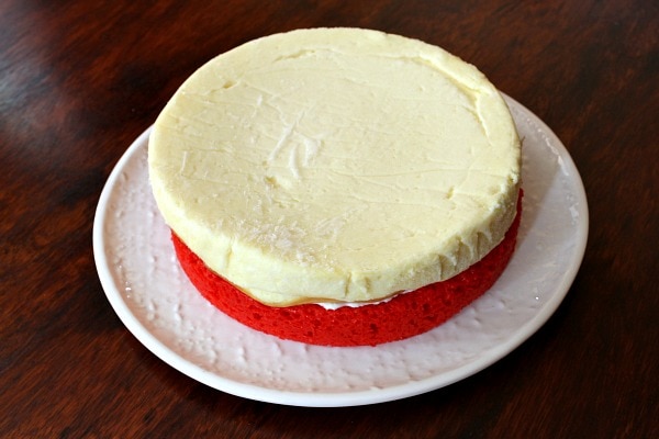 red layer of cake on a white plate topped with a cheesecake layer