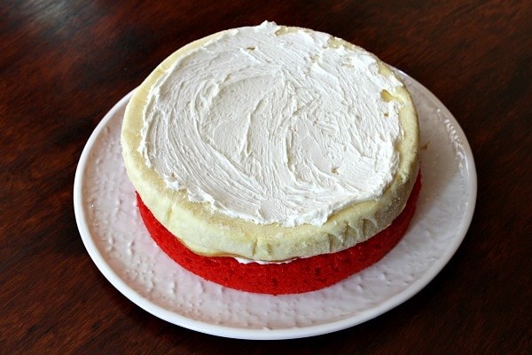 layer of red cake topped with a layer of cheesecake and then frosting on a white plate