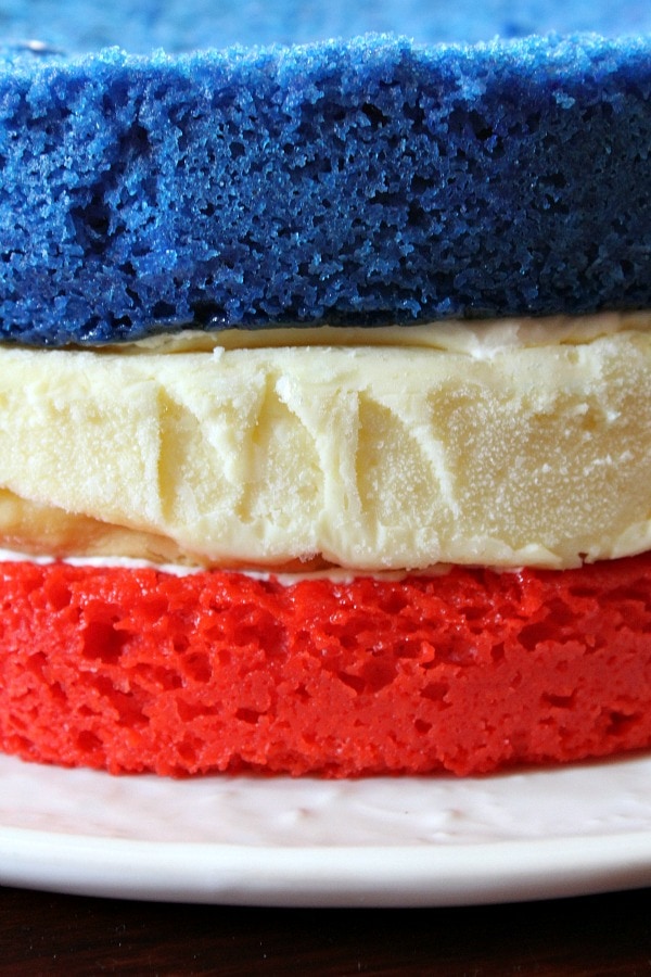 three layers of cake close up- red cake, white cheesecake and blue cake on top