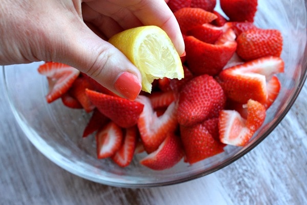 Squeezing lemon onto chopped strawberries in glass bowl