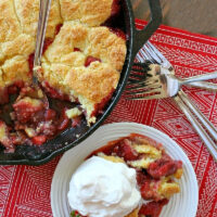 strawberry shortcake skillet cobbler in black skillet with serving of cobbler with cream on the side