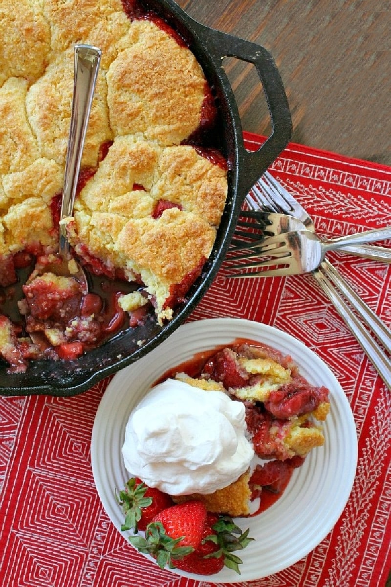 strawberry shortcake skillet cobbler in black skillet with serving of cobbler with cream on the side