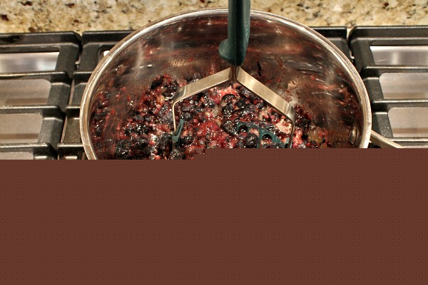 Blueberries being mashed in a saucepan on the stove
