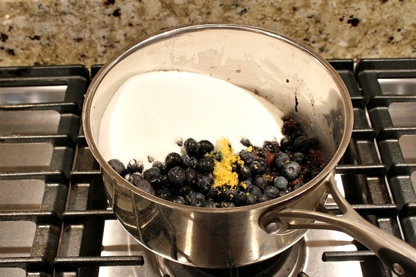 Blueberries, lemon zest and sugar in a saucepan on the stove waiting to be cooked into jam.