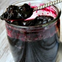 jar of blueberry jam open with a spoon inside and jam on the spoon sitting on the top