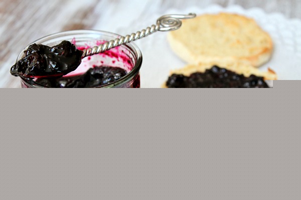Blueberry Refrigerator Jam in a jar with a spoonful of jam sitting on top. English muffin with jam on a plate next to it.