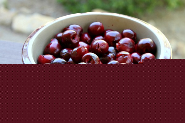 fresh cherries in a round burgundy casserole dish set on a wooden railing