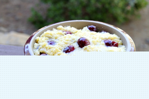 cherry cobbler in a round burgundy casserole dish sitting on a wooden railing - ready to be put into the oven