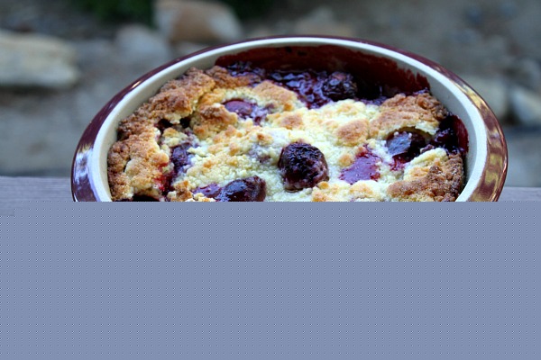 Cherry cobbler in a round burgundy casserole dish sitting on a wooden railing