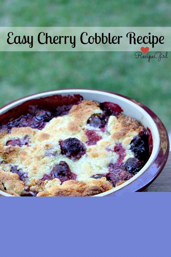 Cherry Cobbler in a round burgundy casserole dish on a wooden railing with green background