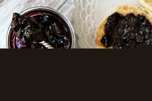 overhead shot of Homemade Blueberry Refrigerator Jam in a jar with a spoonful of jam sitting on top. english muffin with jam on a plate alongside