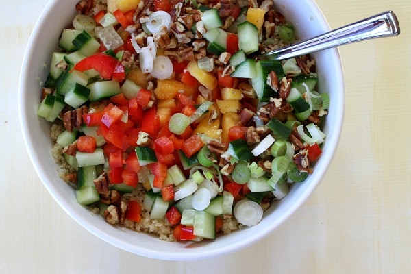 Ingredients for Peach and Pecan Quinoa Salad in a white bowl with a spoon