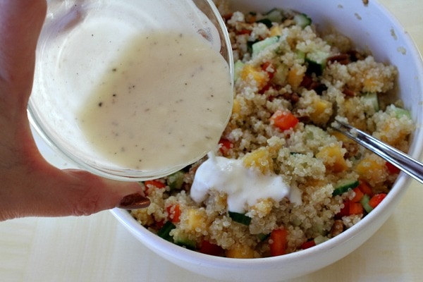 Peach and Pecan Quinoa Salad recipe from RecipeGirl.com #peach #pecan #quinoa #salad #recipe #RecipeGirl Pouring dressing onto Peach and Pecan Quinoa Salad in a white bowl with a spoon