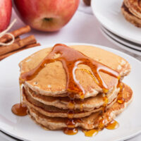stack of apple pie pancakes with syrup on top on white plate