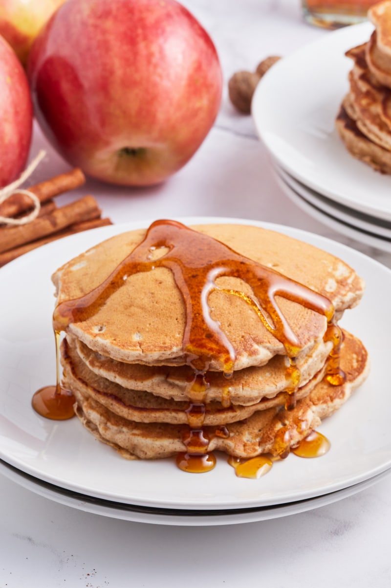 stack of apple pie pancakes with syrup on top on white plate