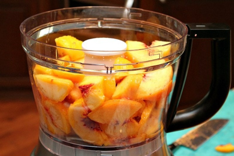 fresh peaches sitting in the bowl of a food processor