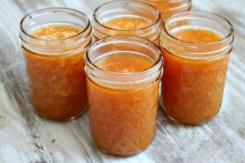 five jars of peach freezer jam without lids sitting on a wooden surface