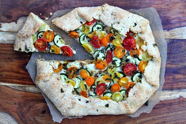 Rustic Tomato and Zucchini Tart on a cutting board with one slice pulled out of it